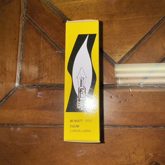 Yellow box packaging for 40 watt 120V clear candelabra bulb displayed on wooden floor with metal pipe.
