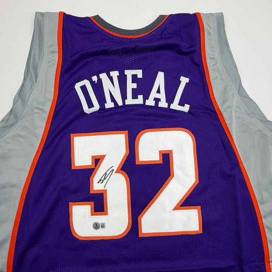 Purple Phoenix Suns basketball jersey with "O'NEAL" and number "32" in white and orange, displayed flat with gray sleeves visible and an autograph on the number.