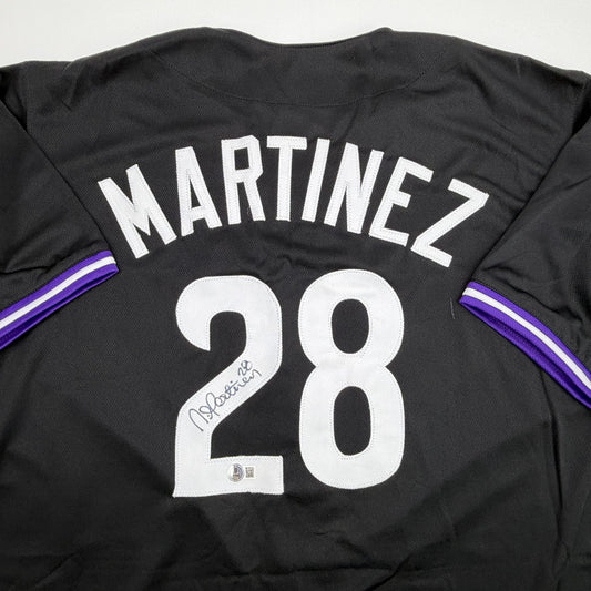 Back view of black baseball jersey with "MARTINEZ" and number 28 in white, purple sleeve stripes, and autographed signature on number.