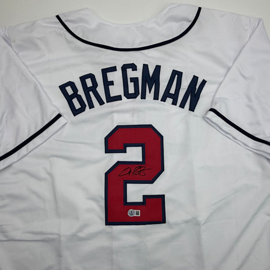 White baseball jersey with "BREGMAN" in navy lettering and red number 2 with signature, displayed flat against gray background.