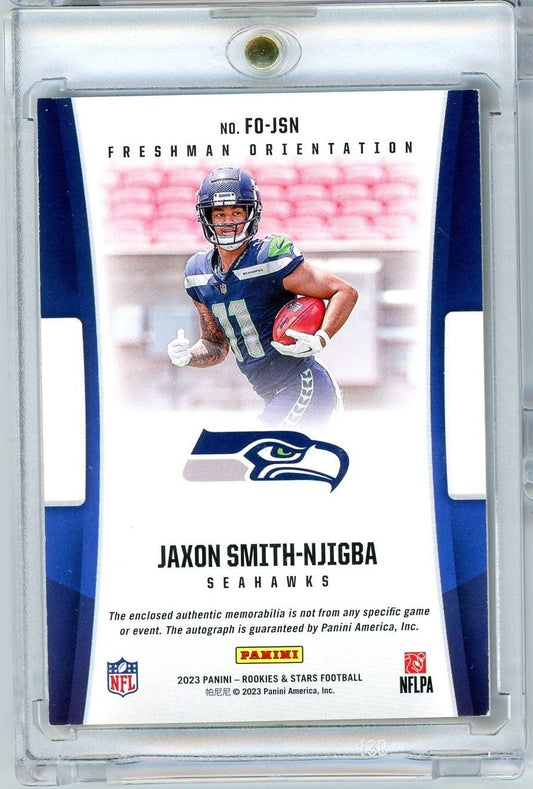 Front of rookie card showing Jaxon Smith-Njigba in Seattle Seahawks uniform holding football against blurred stadium background.