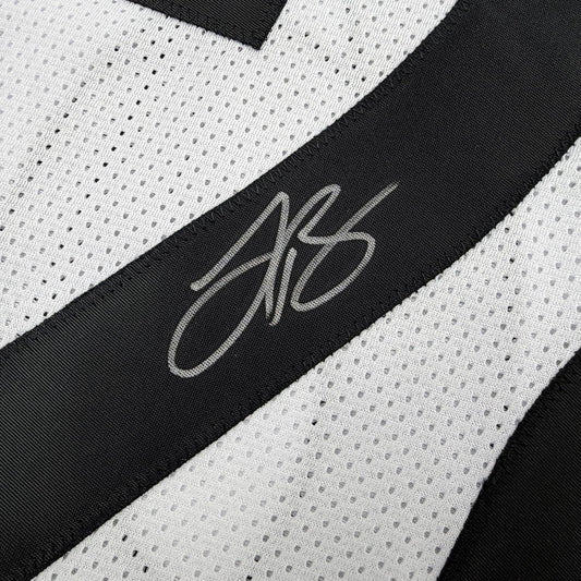 Close-up of black fabric stripe with gray stitched signature on white perforated mesh jersey background.