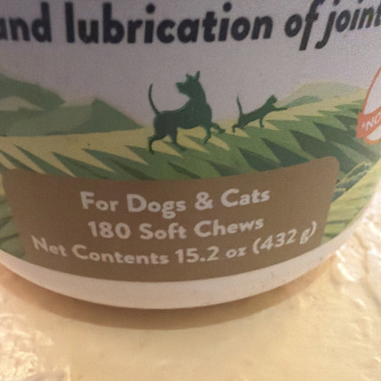 Close-up of product label showing brown band with white text reading "For Dogs & Cats 180 Soft Chews" and "Net Contents 15.2 oz (432 g)" against green illustrated landscape background.