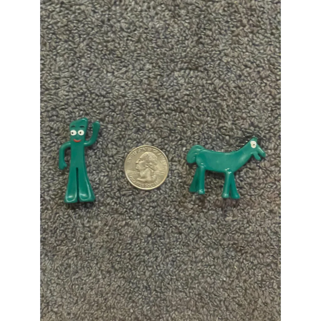 Miniature green Gumby and Pokey plastic figurines beside a quarter for scale on gray carpet