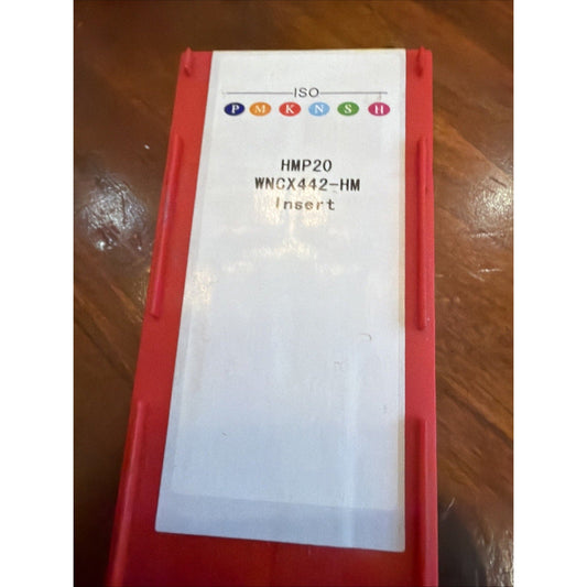 Red plastic packaging box displaying white label with ISO PMKNS logo and product details HMP20 WNCX442-HM Insert text, photographed from above on brown leather surface.