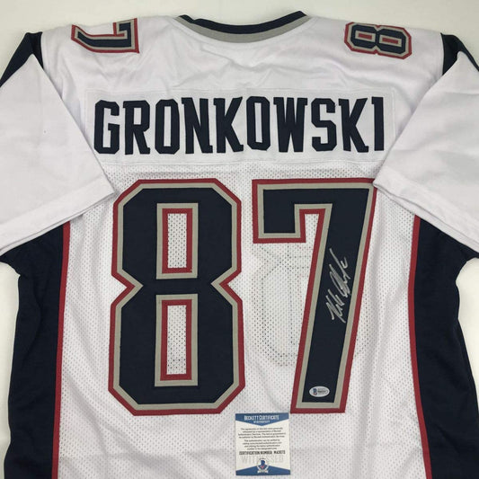 Back view of white New England Patriots football jersey with "GRONKOWSKI" and number 87 in navy and red, featuring Beckett authentication label.