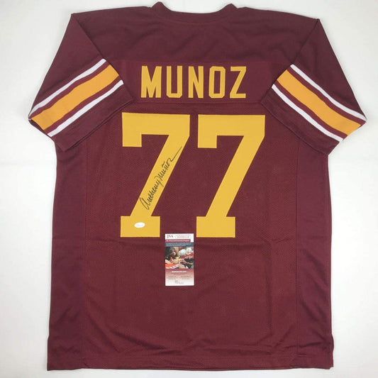Back view of maroon college football jersey with "MUNOZ" and number 77 in gold lettering, signed in black ink, with JSA authentication certificate attached.