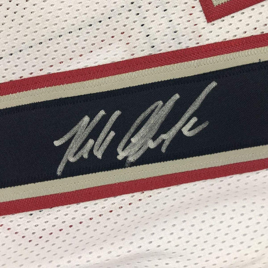 Close-up of embroidered signature on dark navy stripe of white mesh football jersey with red and cream trim.