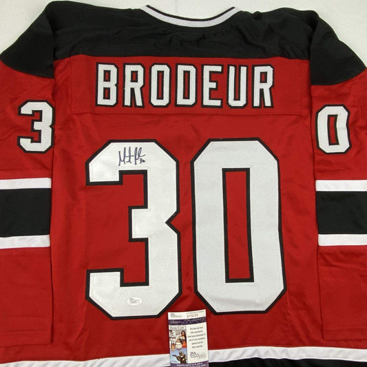Autographed red New Jersey Devils hockey jersey number 30 with "BRODEUR" nameplate and JSA authentication certificate visible.