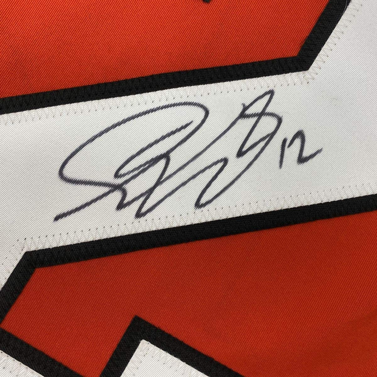 Close-up of autographed white stripe on red and black hockey jersey showing handwritten signature in dark ink.