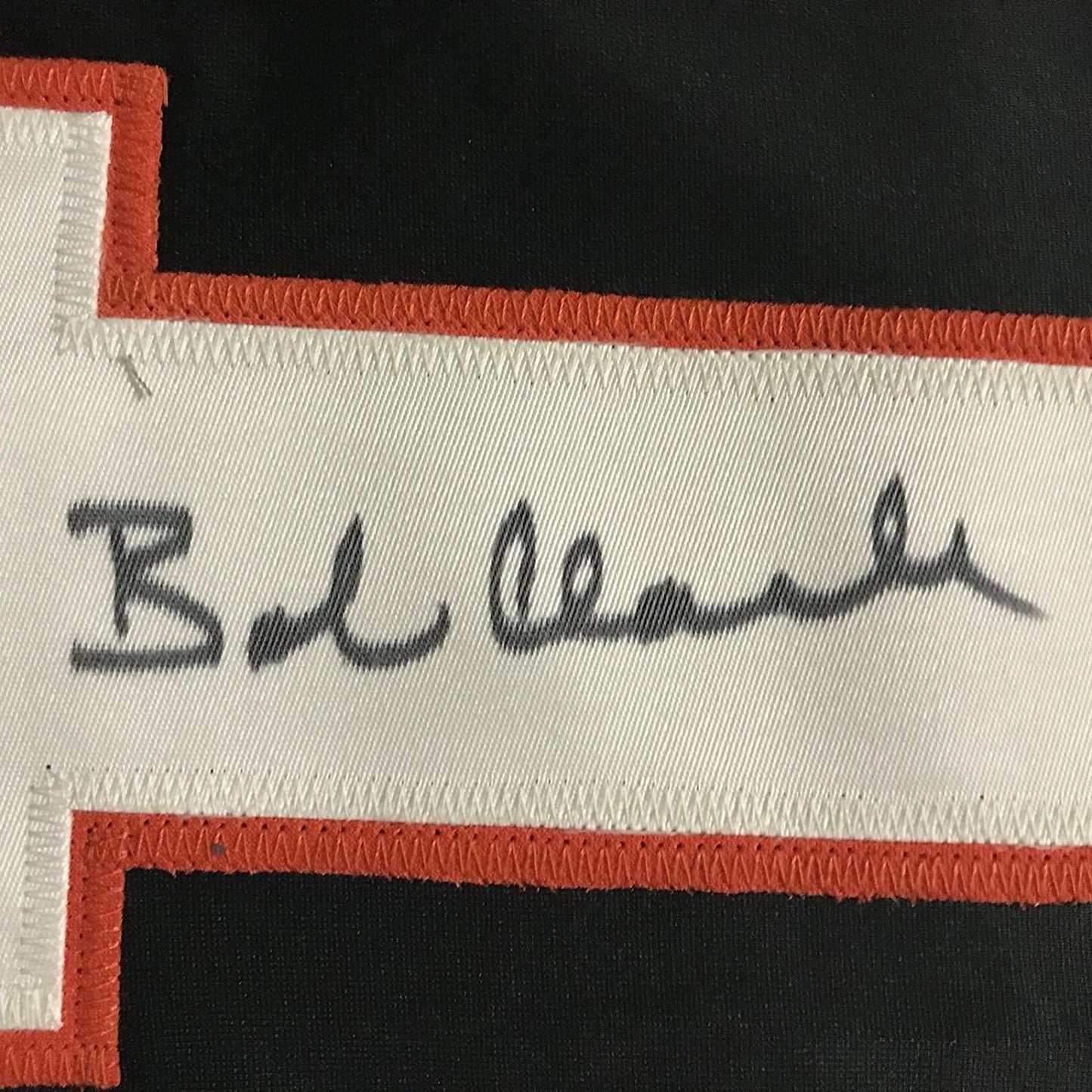 Close-up of handwritten signature on white fabric strip with red stitched borders, reading "B. Clarke".