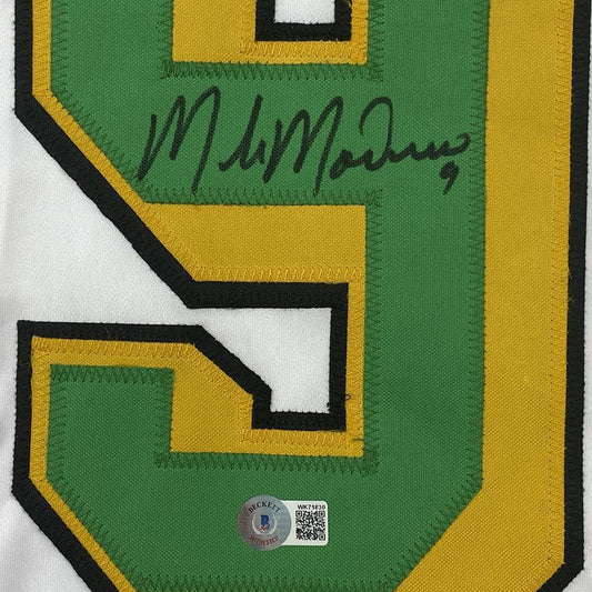 Close-up of a white jersey's green and gold number 9 bearing a black ink signature and a Beckett sticker.