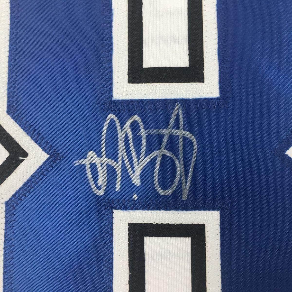 Close-up of autographed signature in silver ink on blue hockey jersey fabric with white and black striping.