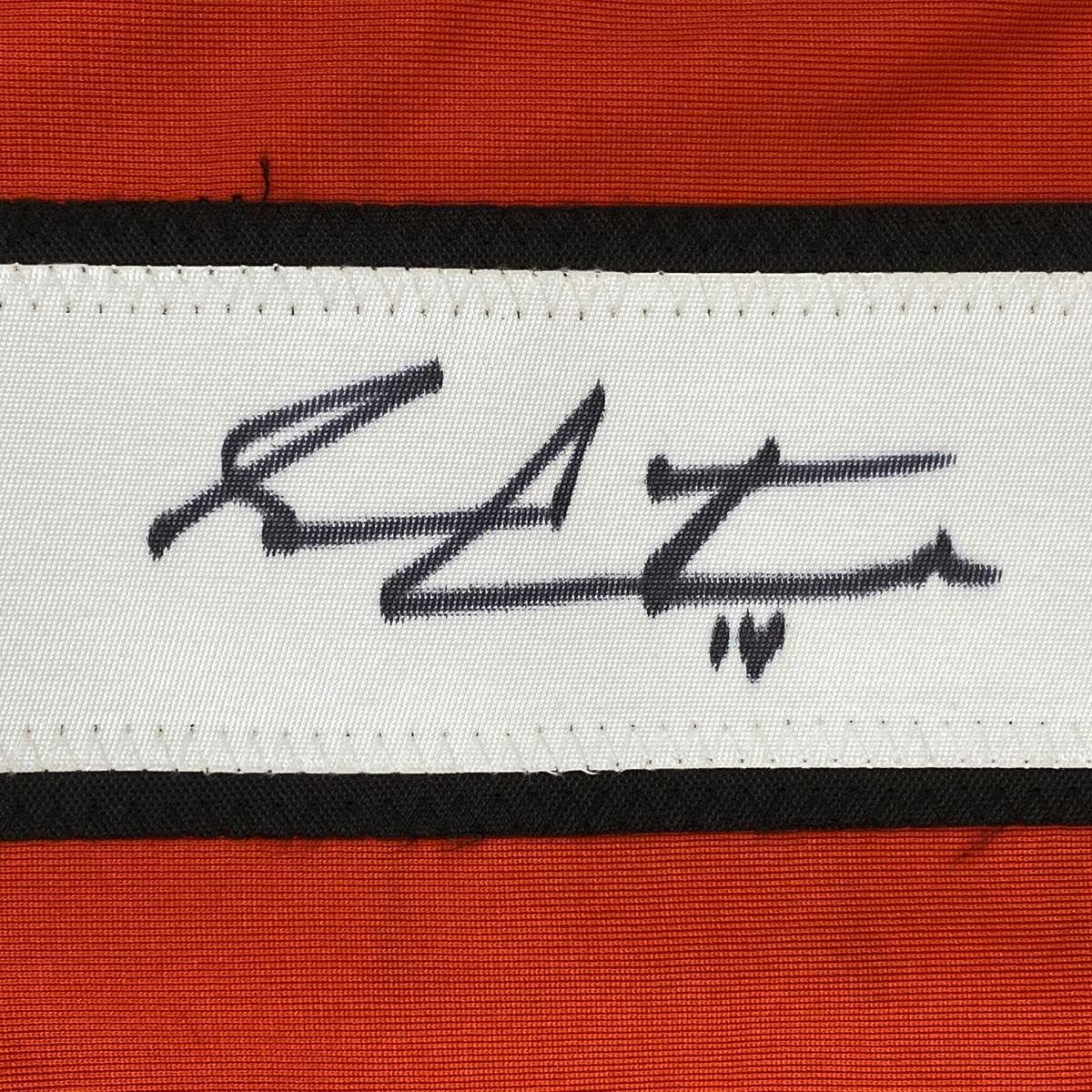 Close-up of handwritten signature on white fabric stripe between black and orange horizontal bands.