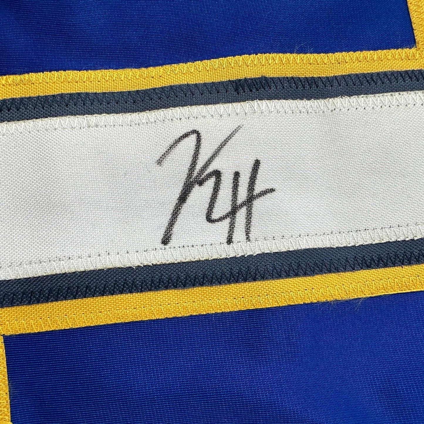 Close-up of handwritten signature on white stripe of blue, yellow, and navy striped hockey jersey.