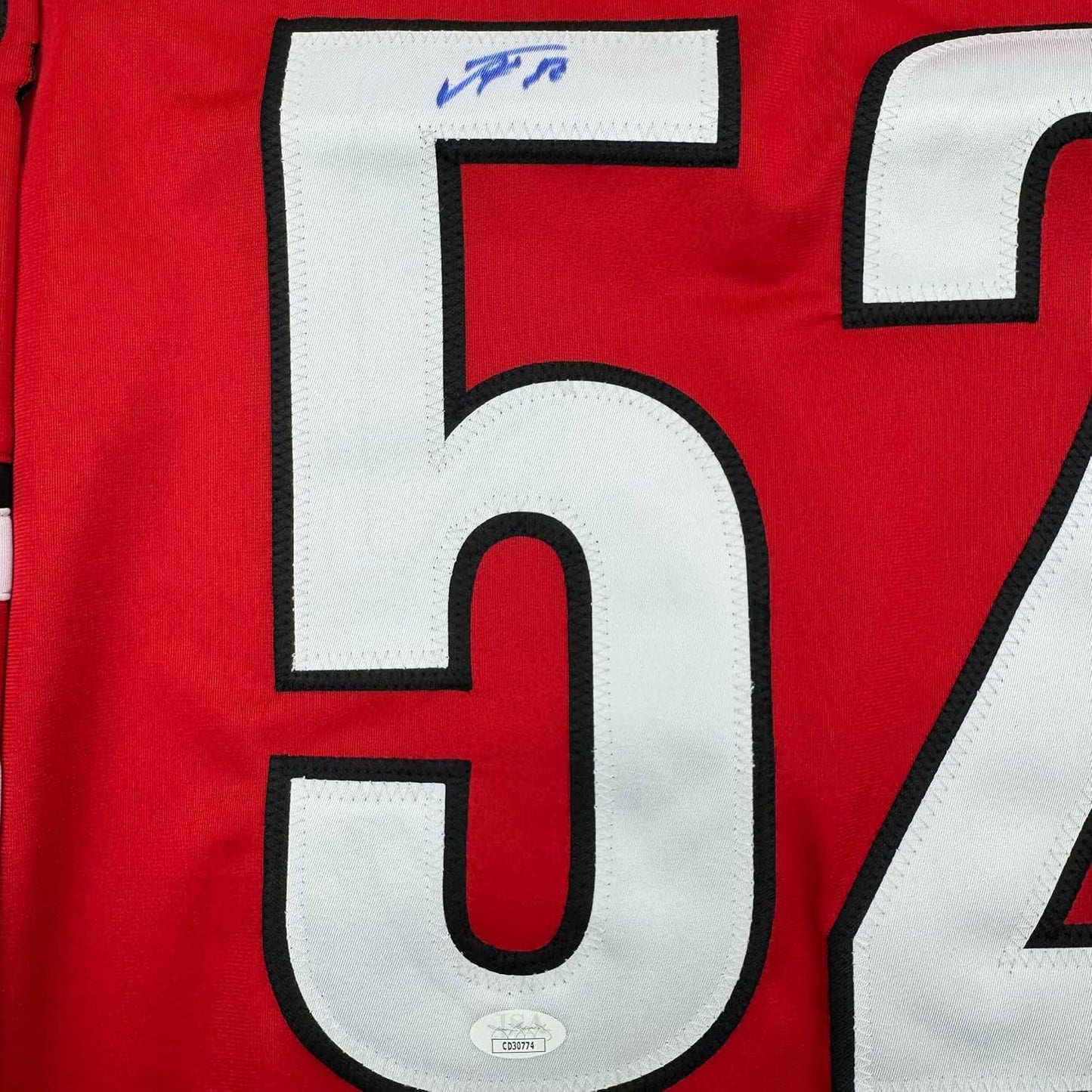Close-up of white number 5 with black outline on red hockey jersey fabric, with blue autograph visible above.
