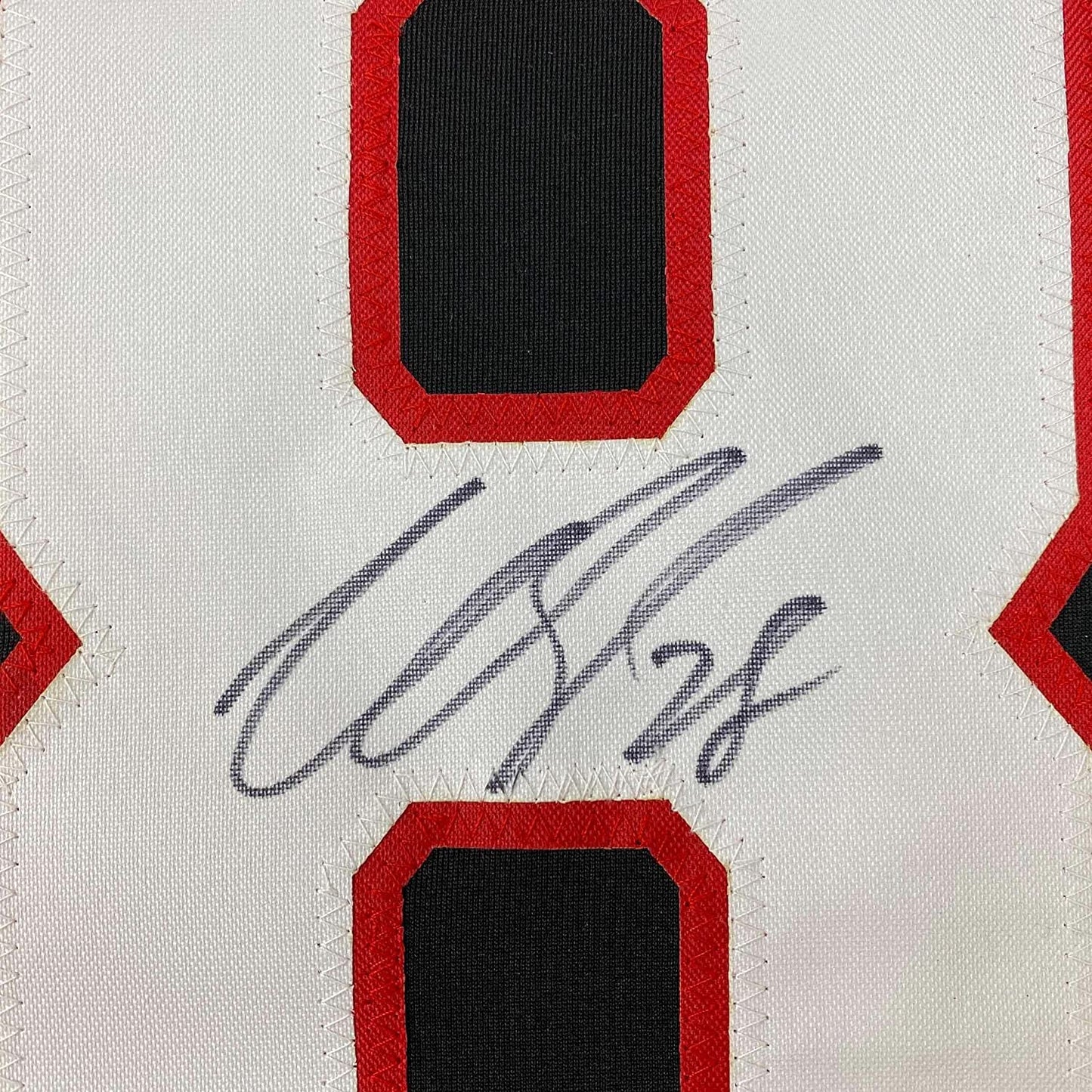 Close-up of handwritten autograph in dark blue ink on white fabric with red and black bordered sections.
