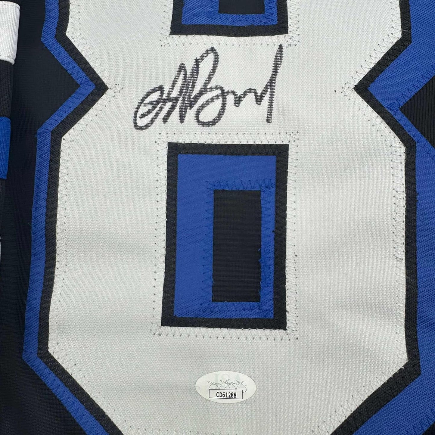 Close-up of signed white jersey chest with blue and black geometric pattern and JSA authentication sticker.