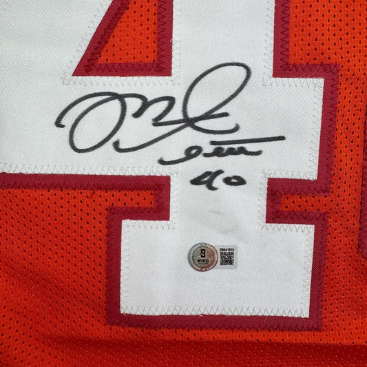 Close-up of signed red and white football jersey showing black handwritten autograph and Beckett authentication hologram sticker.