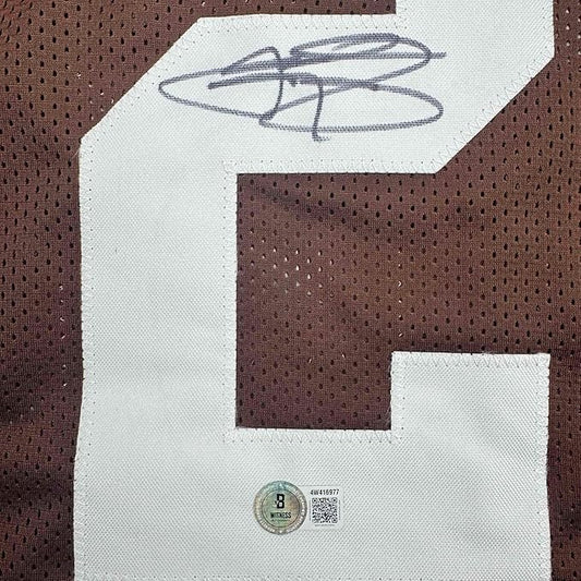 Close-up of handwritten signature in blue ink on white fabric with authentication sticker and QR code visible below.