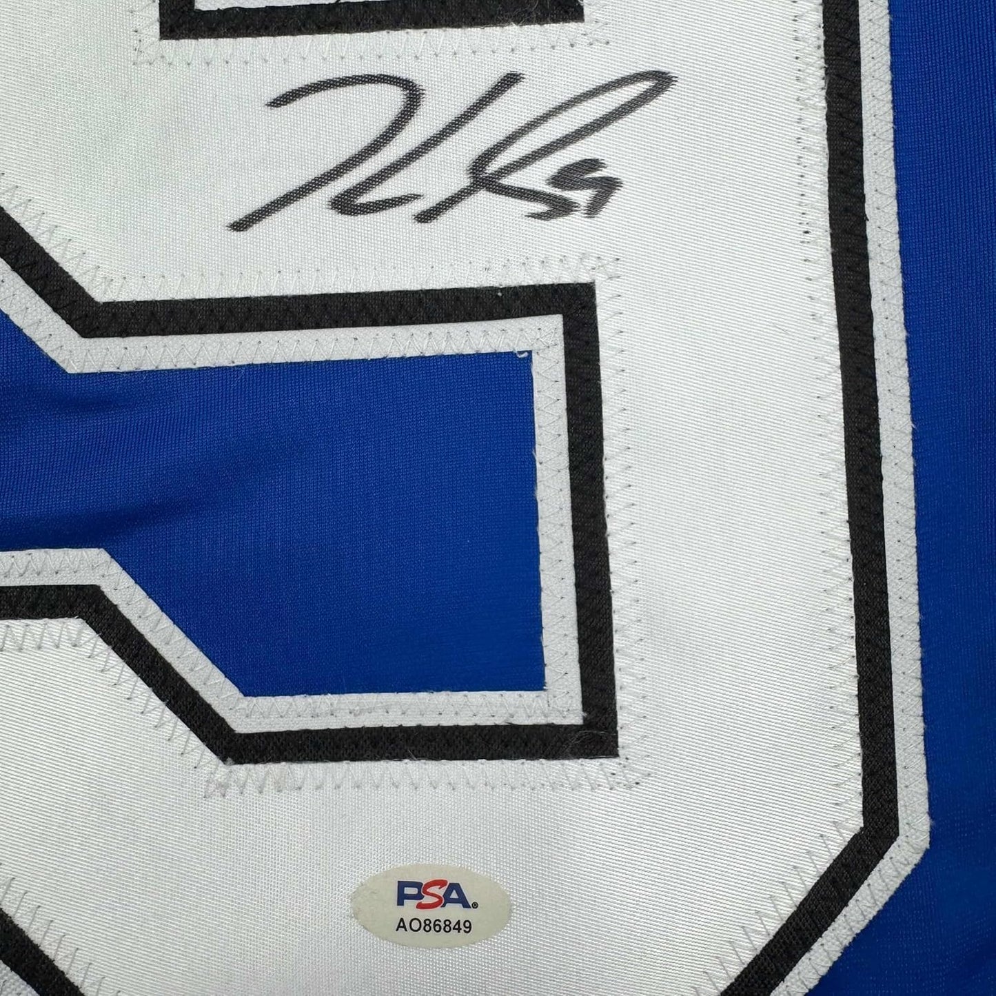 Close-up of autographed blue and white hockey jersey showing handwritten signature and PSA authentication sticker.