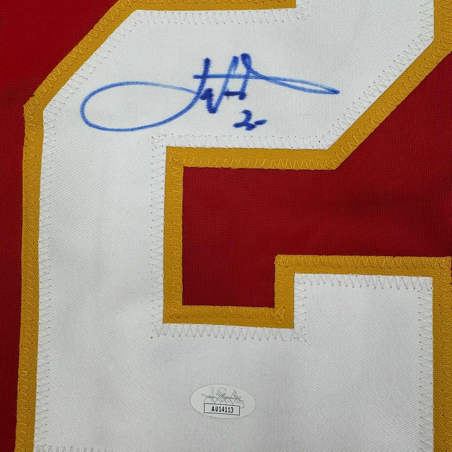 Close-up of blue autograph signature on white jersey panel with gold and red trim, JSA authentication sticker visible below.