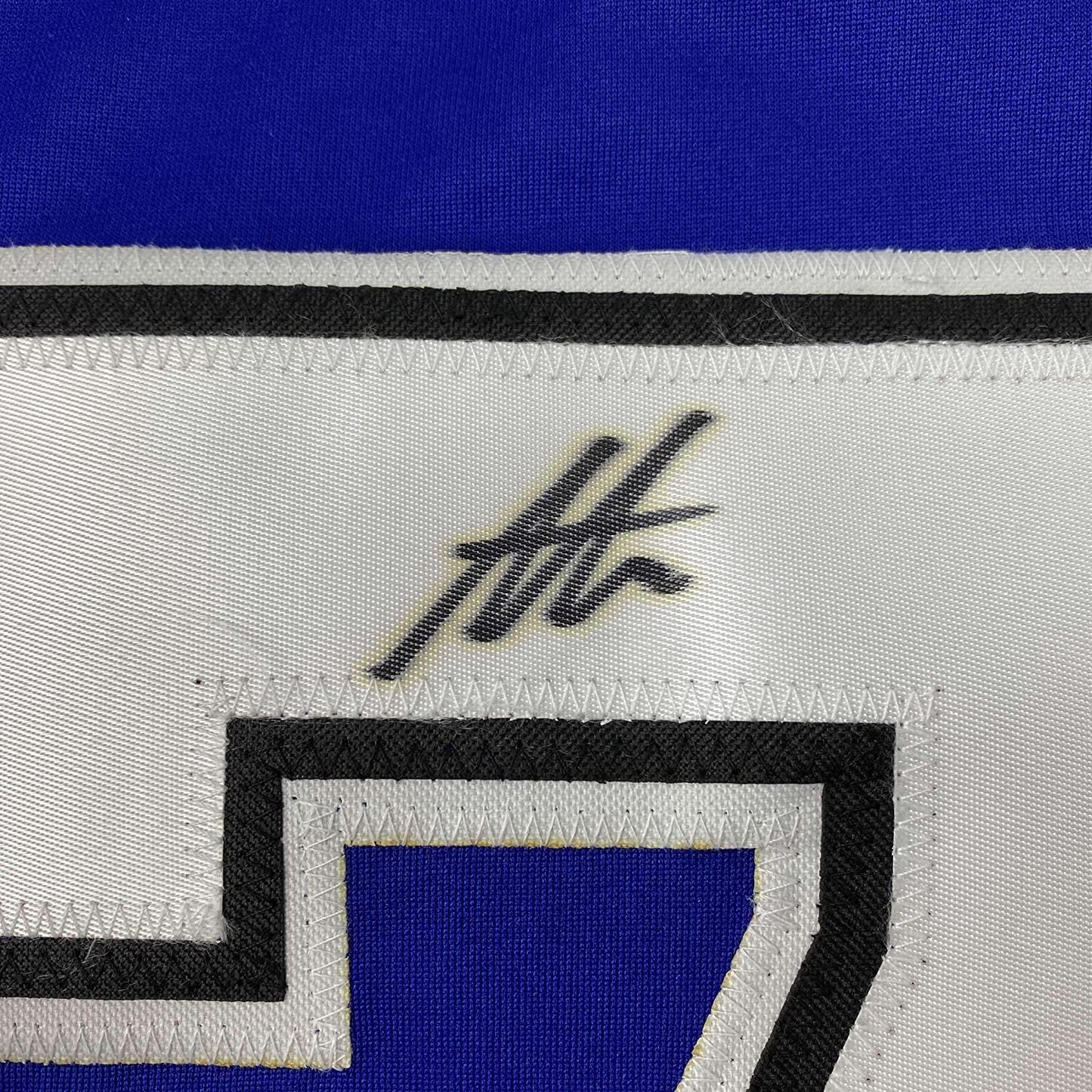 Close-up of blue hockey jersey showing black autographed signature and striped fabric trim detail.
