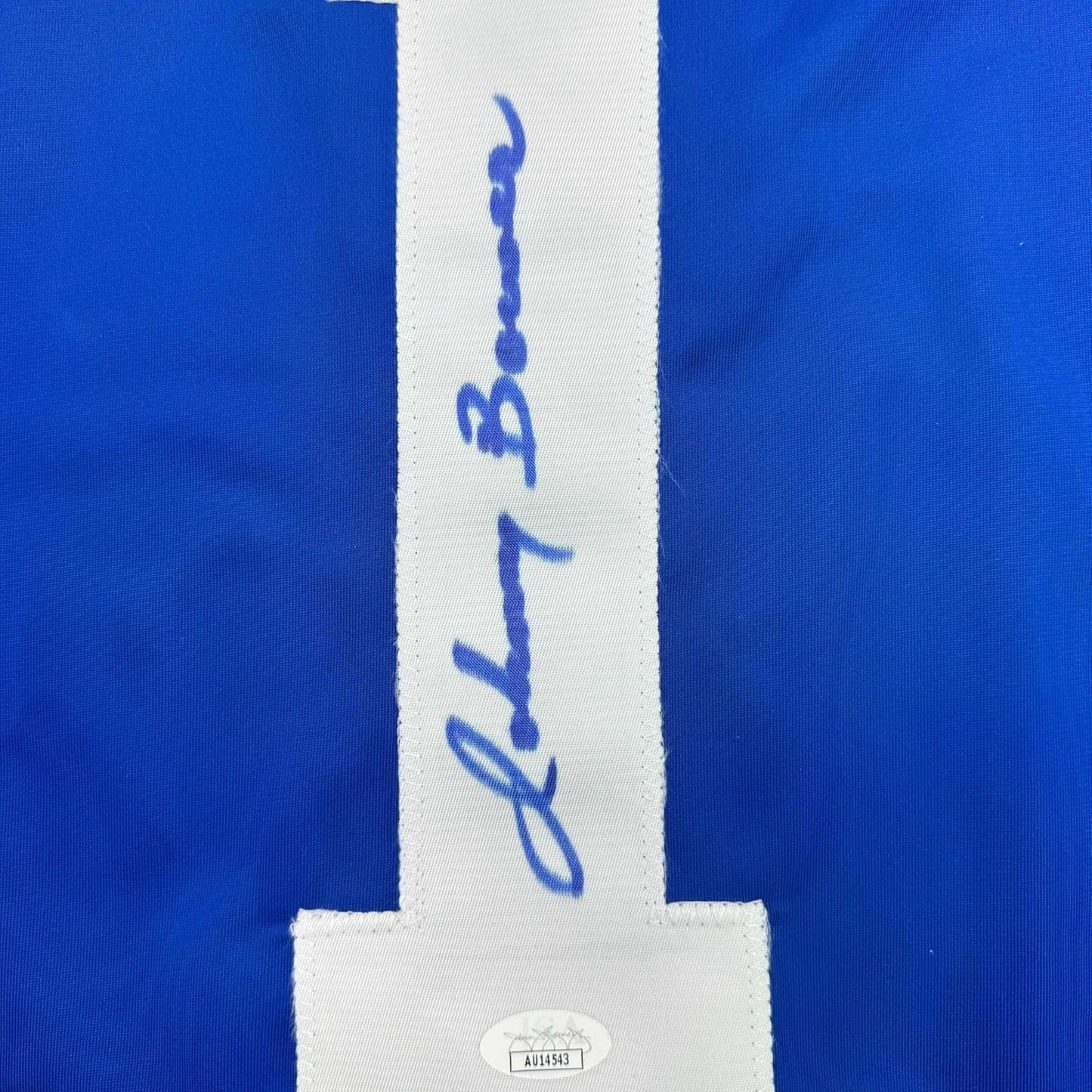 Close-up of white center stripe on blue jersey showing handwritten signature and authentication hologram label.