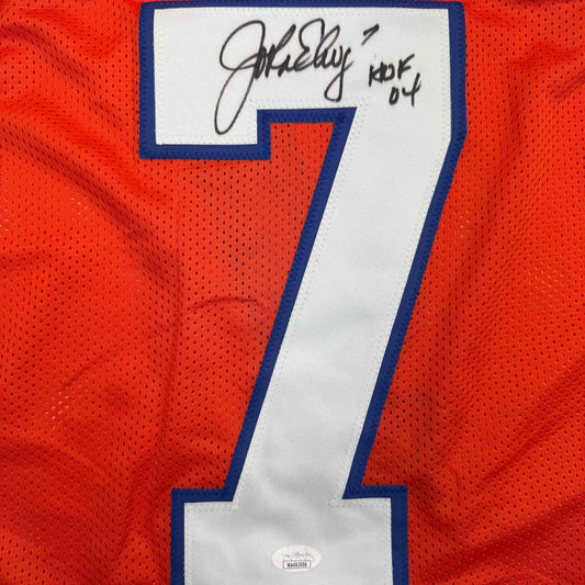 Close-up of signed orange jersey number 7 with blue trim and handwritten autograph on white nameplate.