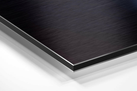 Close-up angled view of layered Dibond panel showing brushed black top surface with silver aluminum edges and white base layer.