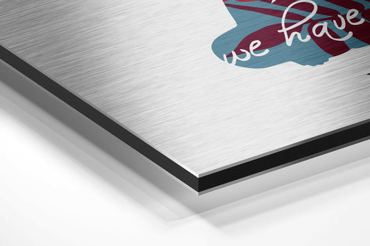 Close-up angled view of brushed aluminum panel edge showing layered construction with black border and white surface, partial blue and maroon design visible at top.