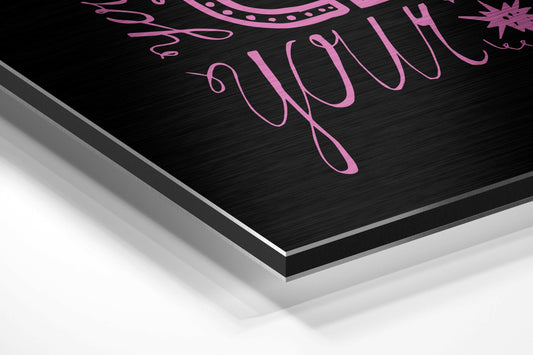 Close-up angled view of black brushed aluminum wall art with pink hand-lettered script text, showing layered edge detail.
