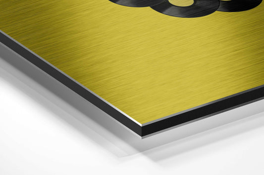 Close-up angled view of layered brushed aluminum dibond panel showing yellow brushed surface with black and gray edge layers.