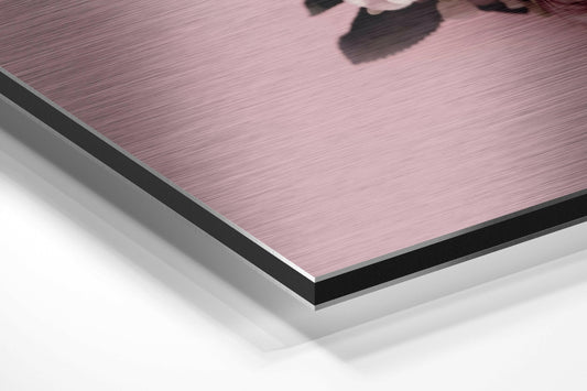 Close-up angle view of layered composite material showing brushed pink aluminum surface with black edge trim and white backing layer.