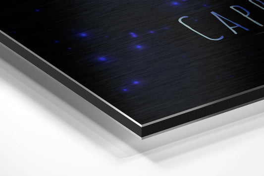 Angled perspective view of layered brushed aluminum dibond wall art showing black textured surface with blue brushstroke design and blue LED accent lights.