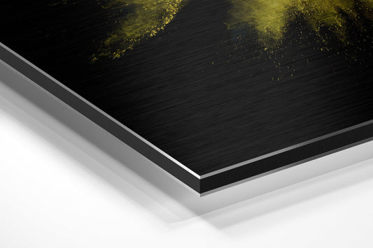 Close-up angled view of layered Dibond wall art showing black brushed aluminum surface with yellow and pink powder burst design, white backing layer visible.