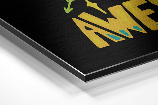Close-up angled view of yellow and teal motivational text on black brushed aluminum dibond with silver edge detail.