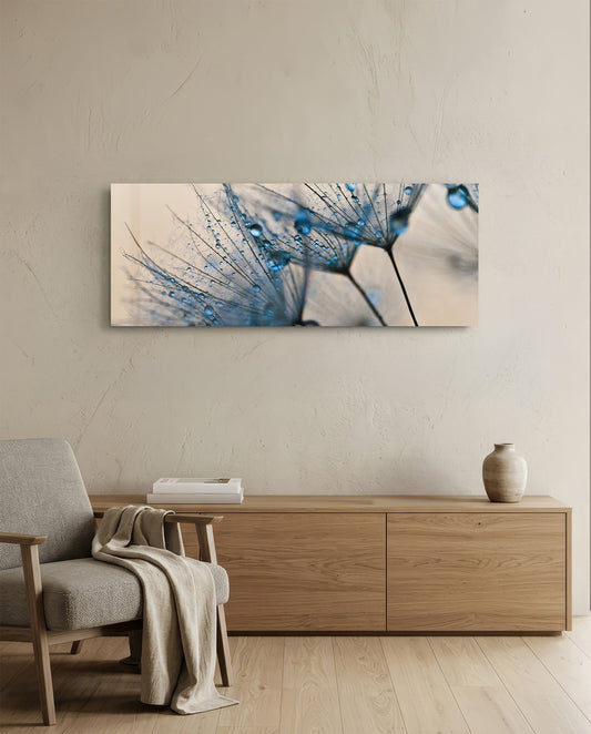 Horizontal glass wall art displaying blue-tinted dandelion seeds with water droplets, hung above wooden furniture in a minimalist interior.