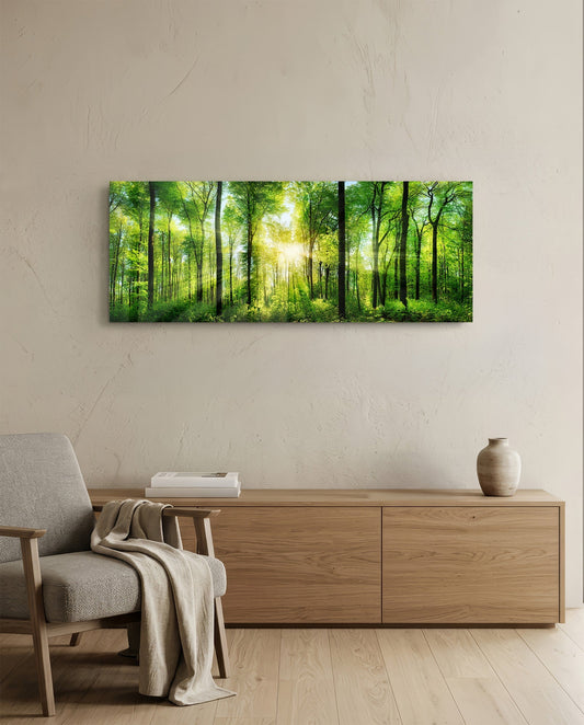 Horizontal glass forest artwork hung above wooden furniture in a minimalist interior, showing sunlit green trees with bright center light.