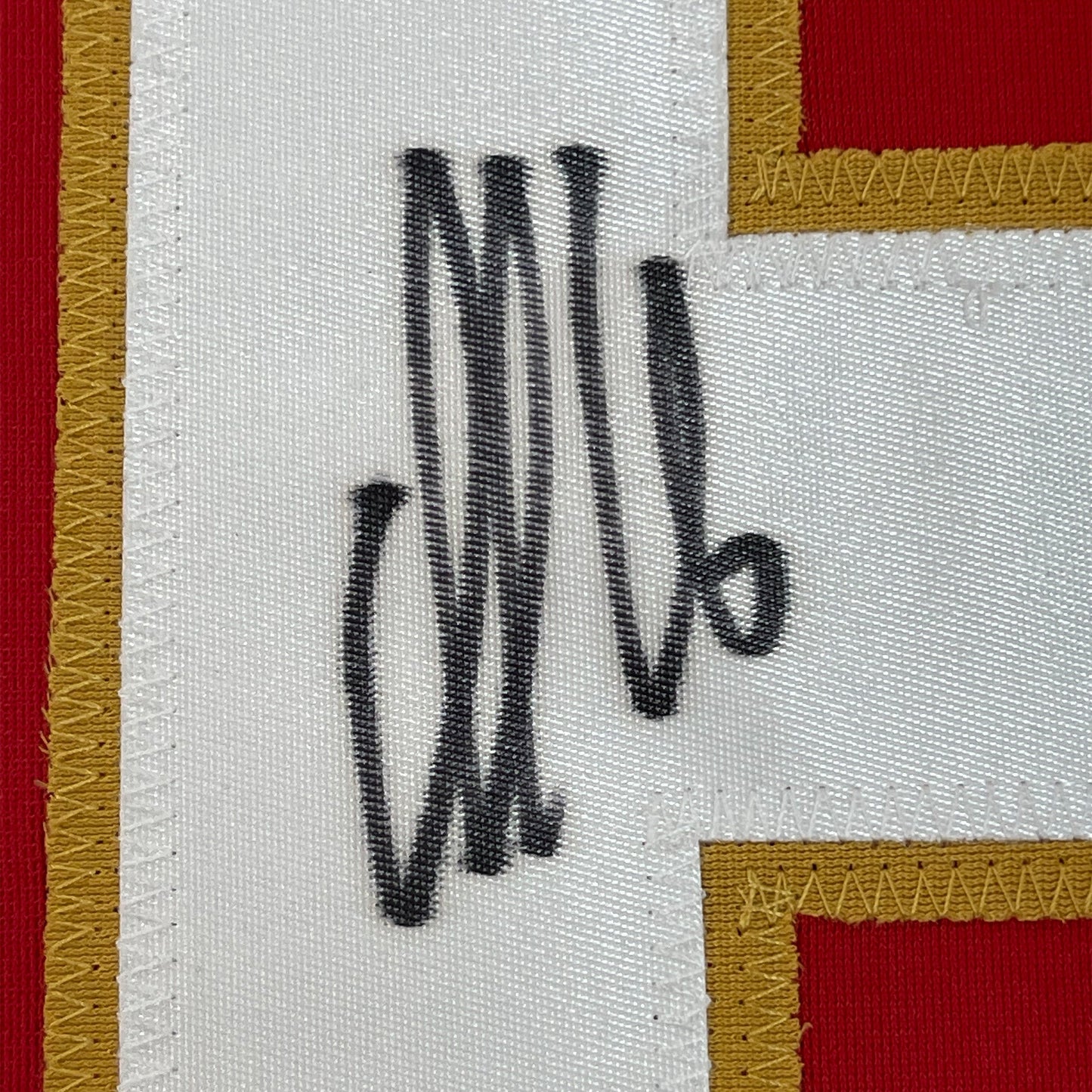 Close-up of black handwritten signature on white fabric with red and gold trim borders.