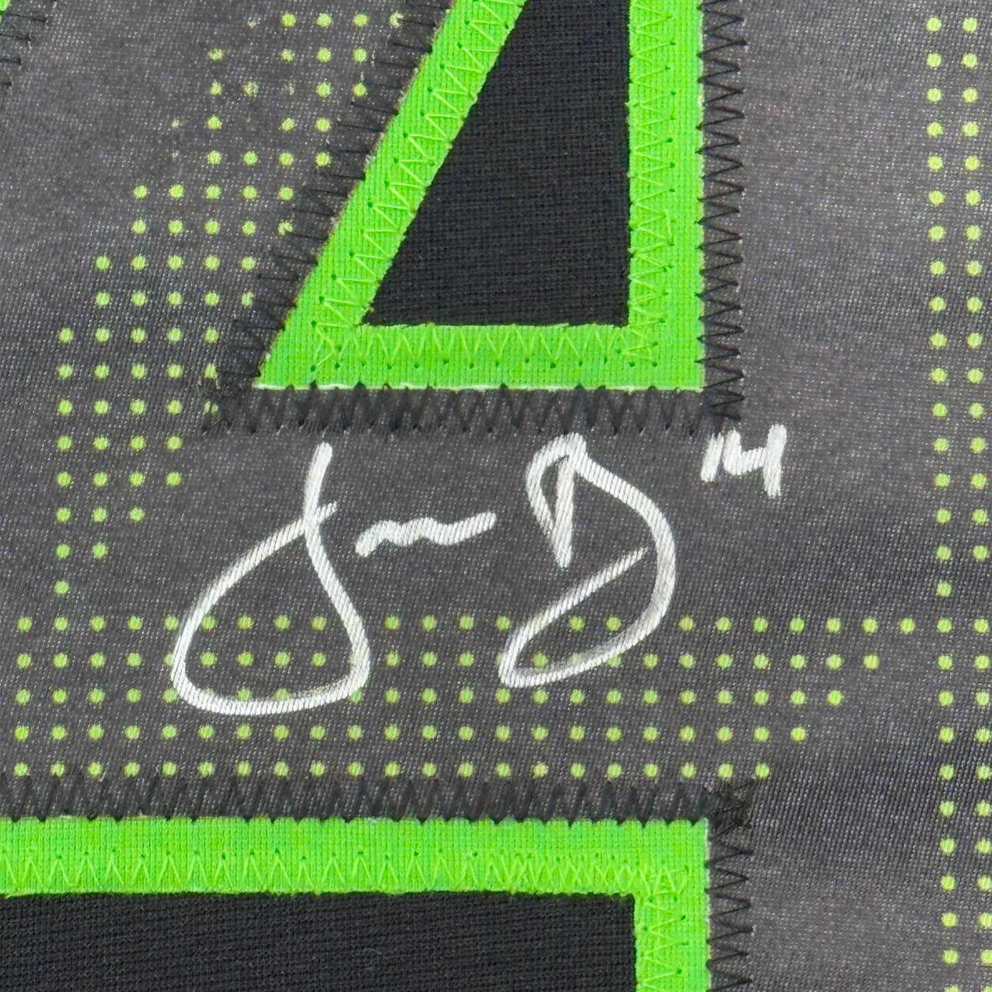 Close-up of neon green binding trim and white signature on dark grey jersey fabric with yellow dot pattern.