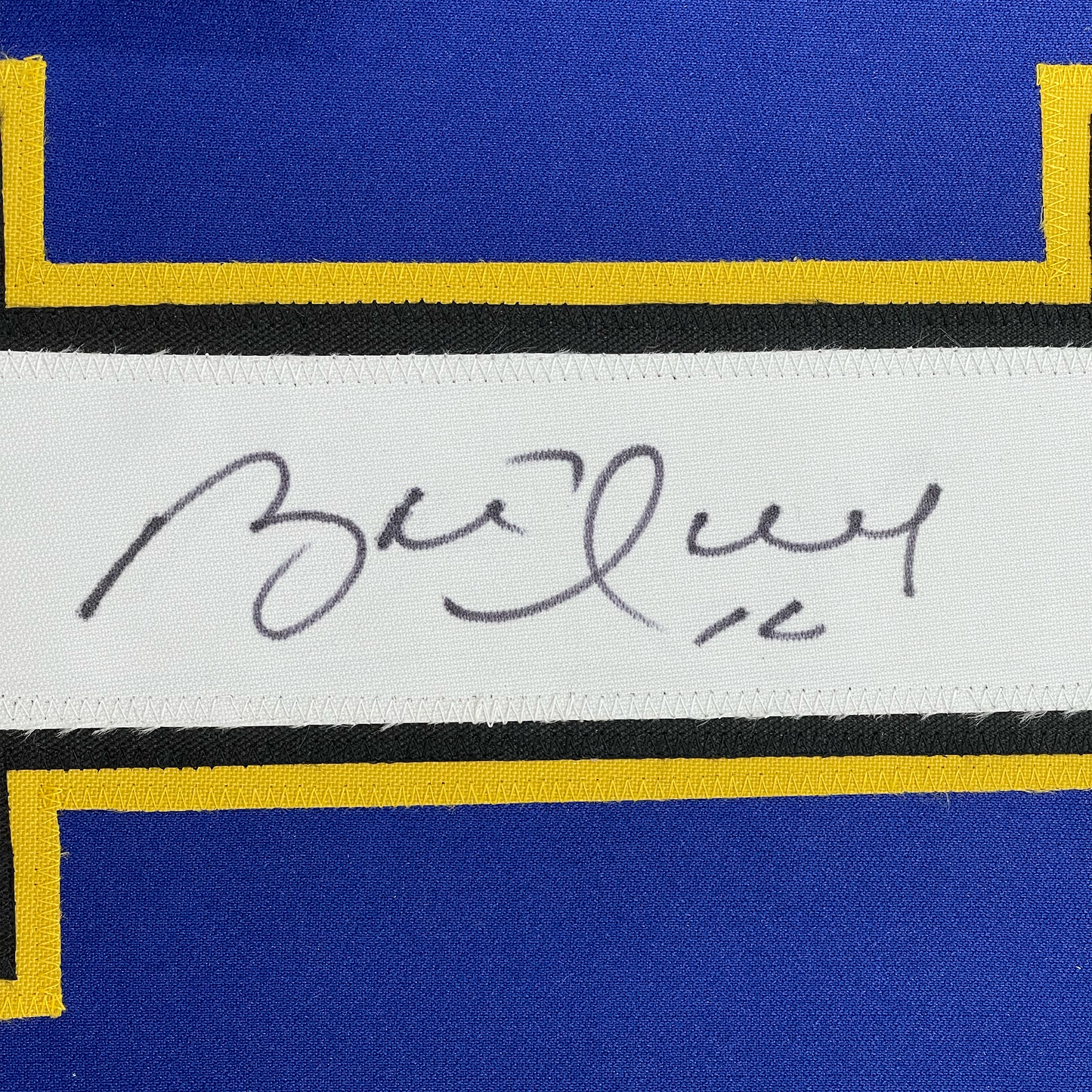 Close-up of handwritten signature on white label strip between blue and yellow striped jersey fabric.