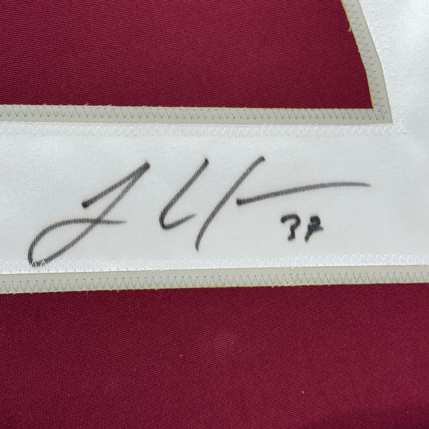 Close-up of handwritten signature on white fabric strip between maroon and cream-colored jersey sections.