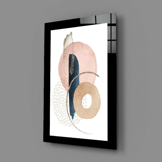 Framed glass wall art displaying abstract composition with pink oval, navy stripe, tan ring, and gold accents on white background, angled three-quarter view.