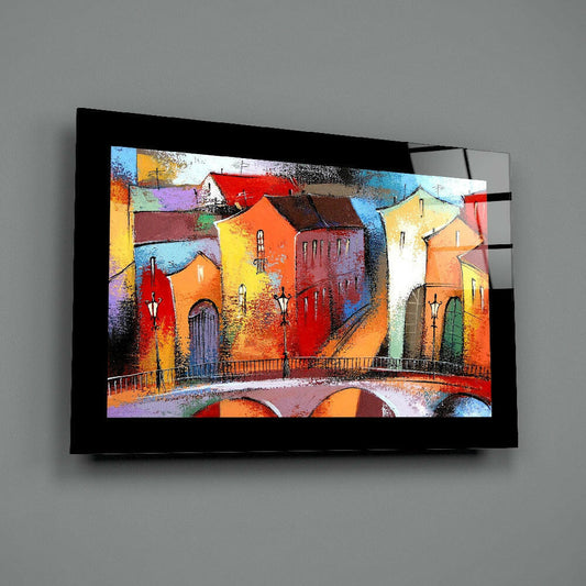 Black-framed glass wall art displaying a vibrant, colorful painting of multi-story buildings with red, orange, yellow, and blue facades, mounted on gray wall.