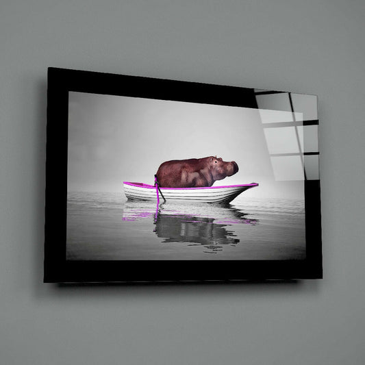 Black-framed glass wall art displaying a brown hippo in a boat with bright pink trim floating on calm gray water.