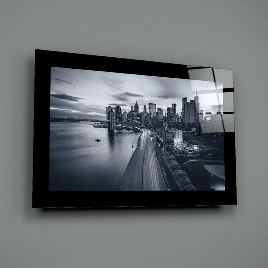 Black-framed glass wall art displaying monochrome Manhattan skyline with highway and waterfront, mounted on gray wall.