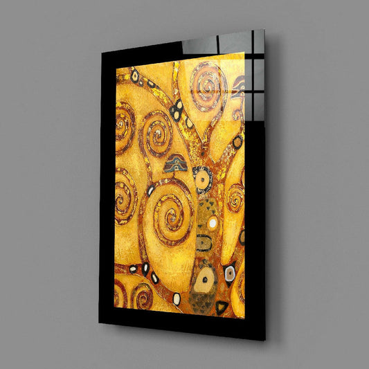 Black-framed glass wall art displaying golden spiral patterns and tree branches mounted at an angle on gray wall.