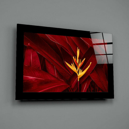 Black-framed glass wall art displaying a vibrant yellow heliconia flower against deep red foliage, mounted on gray wall at an angle.