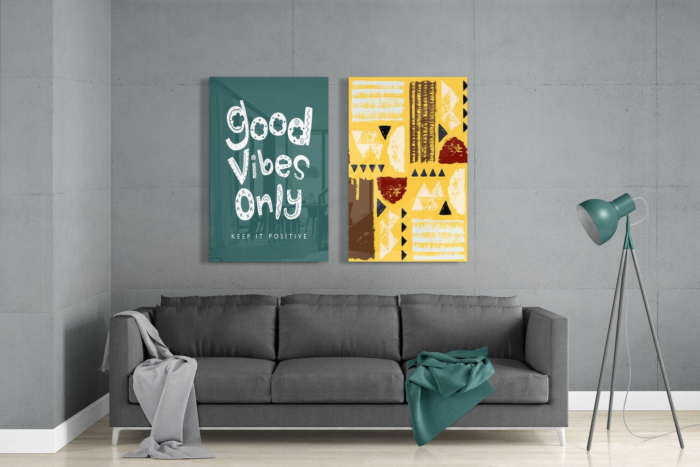 Two framed glass wall art pieces hanging above a gray sofa: teal canvas with white "Good Vibes Only" text and yellow abstract geometric design with brown accents.